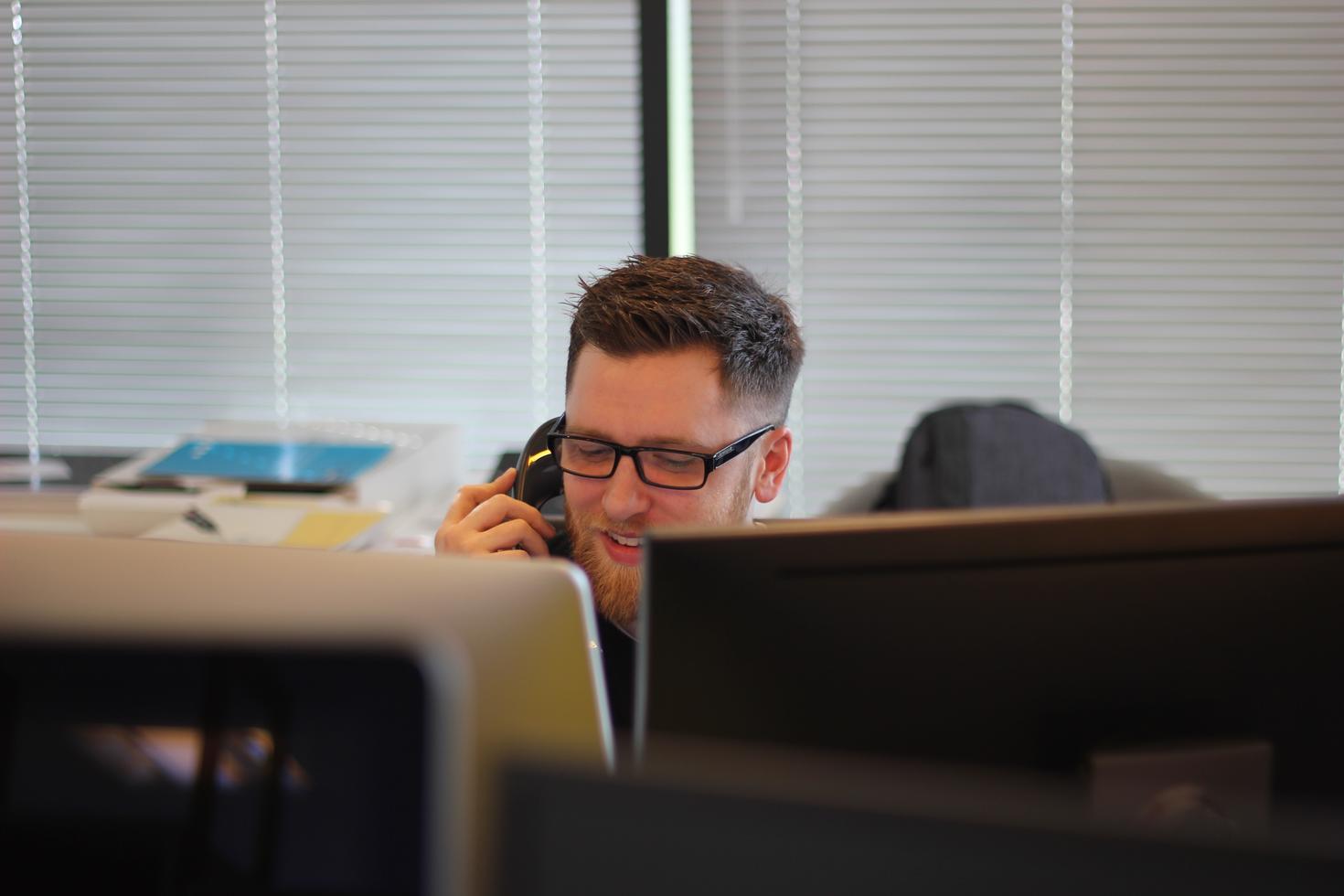 A man sitting behind two monitors talks on the phone