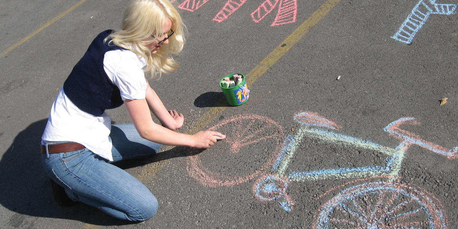 A student drawing a bicycle using chalk on the ground in a parking lot at uOttawa